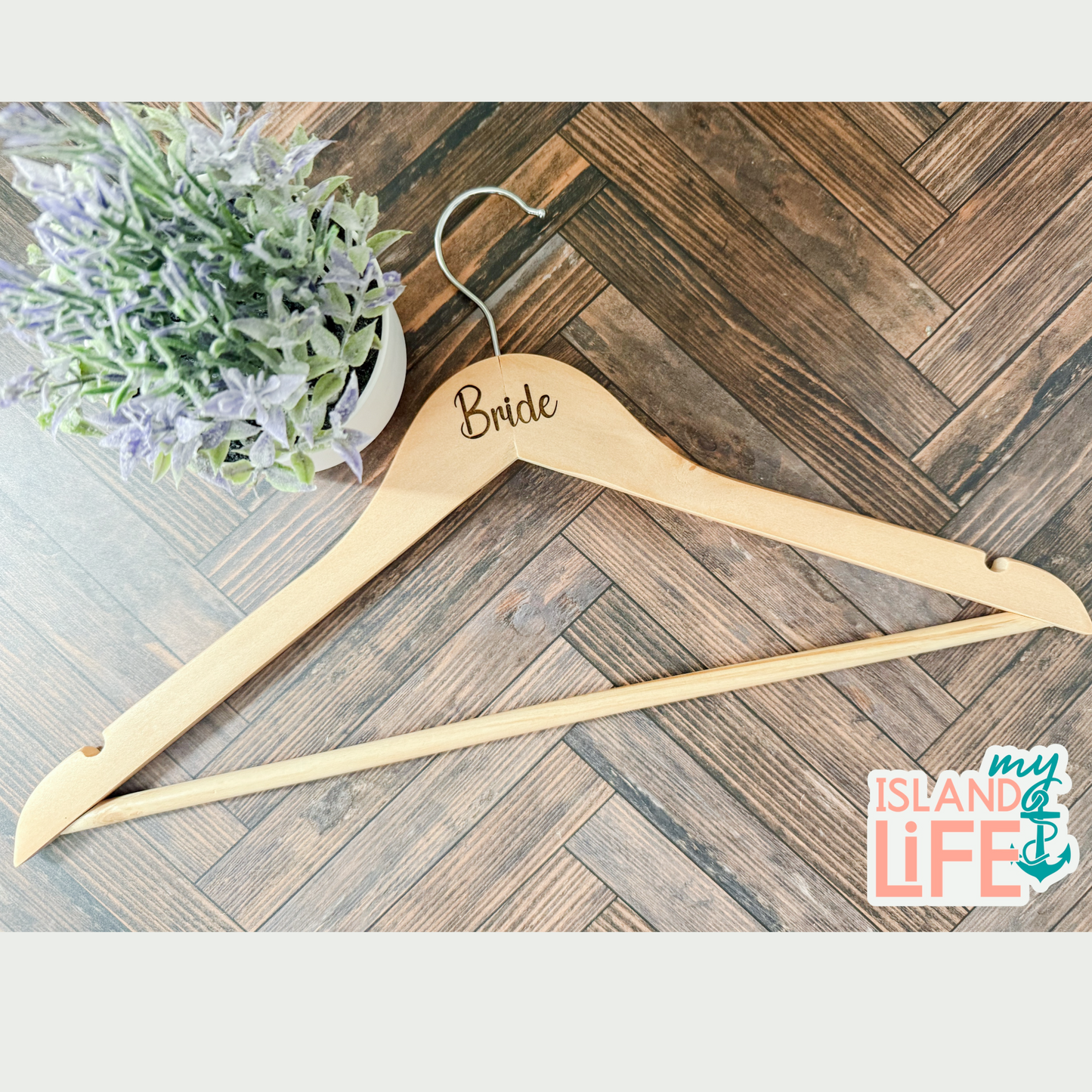 Wooden hanger with 'Bride' engraved on it, placed on a wooden floor with a plant in the background.