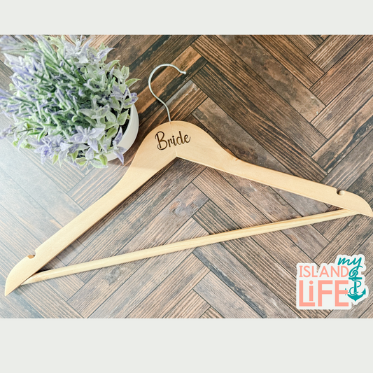 Wooden hanger with 'Bride' engraved on it, placed on a wooden floor with a plant in the background.