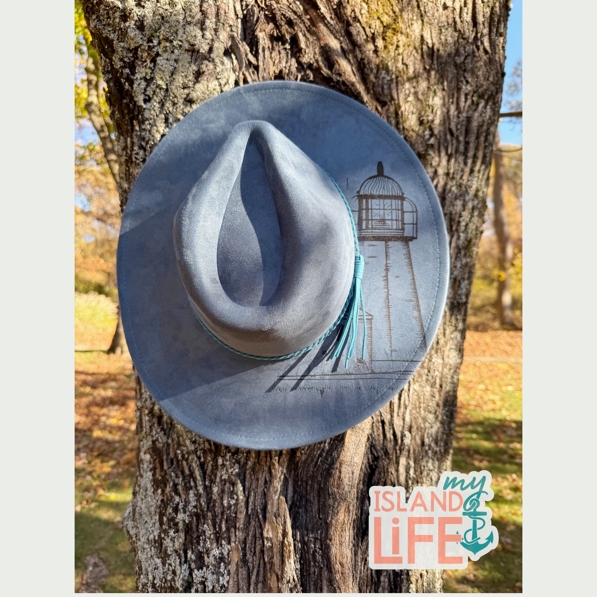 Blue cowboy hat with a lighthouse design on a tree trunk, featuring 'My Island Life' logo.