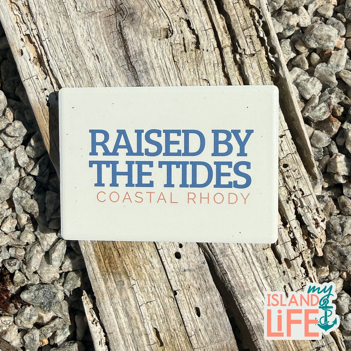 Coastal-themed magnet with 'Raised by the Tides' text on a natural background